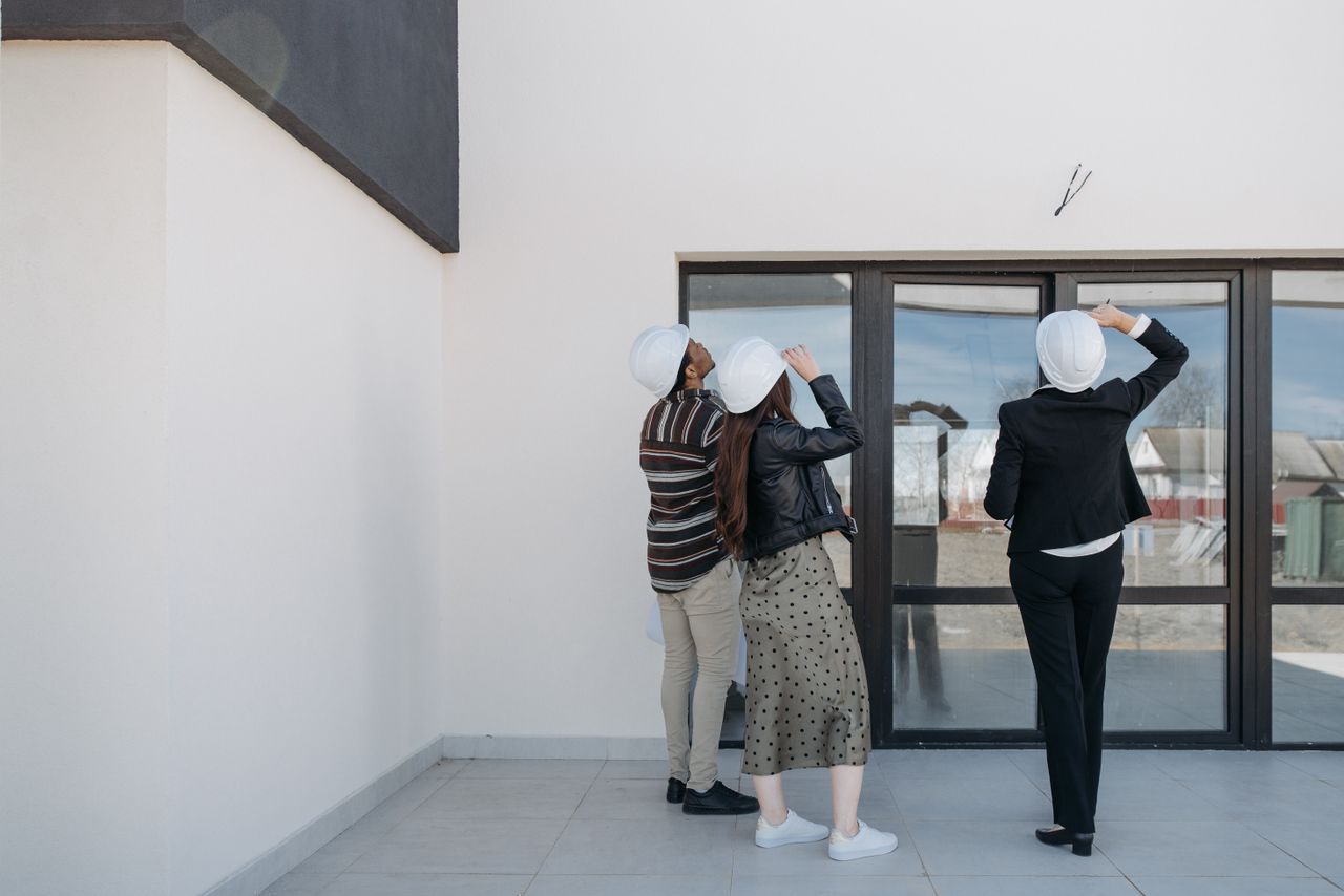 Three architects evaluating exterior building structure, wearing helmets and business attire.